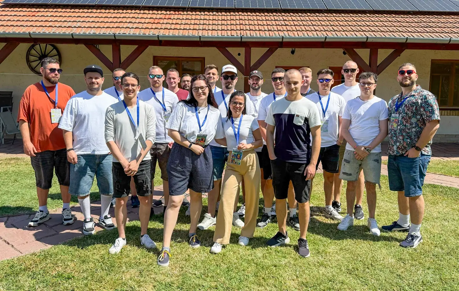 A CodeYard csapata csoportképen egy napsütéses nyári csapatprogramon, egy vidéki ház előtti füves udvaron.